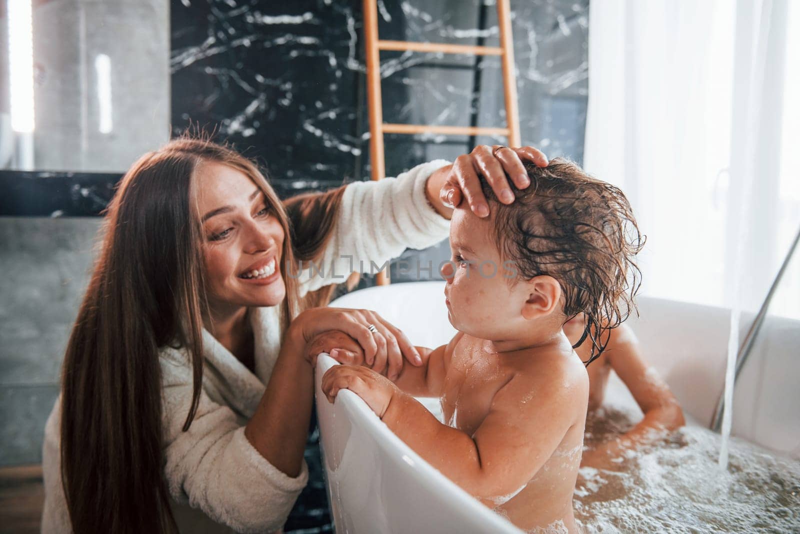 Young mother helps her son and daughter. Two kids washing in the bath.