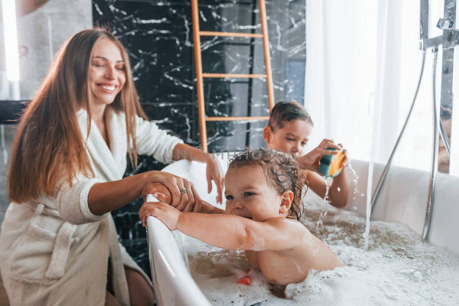 Young mother helps her son and daughter. Two kids washing in the bath by Standret