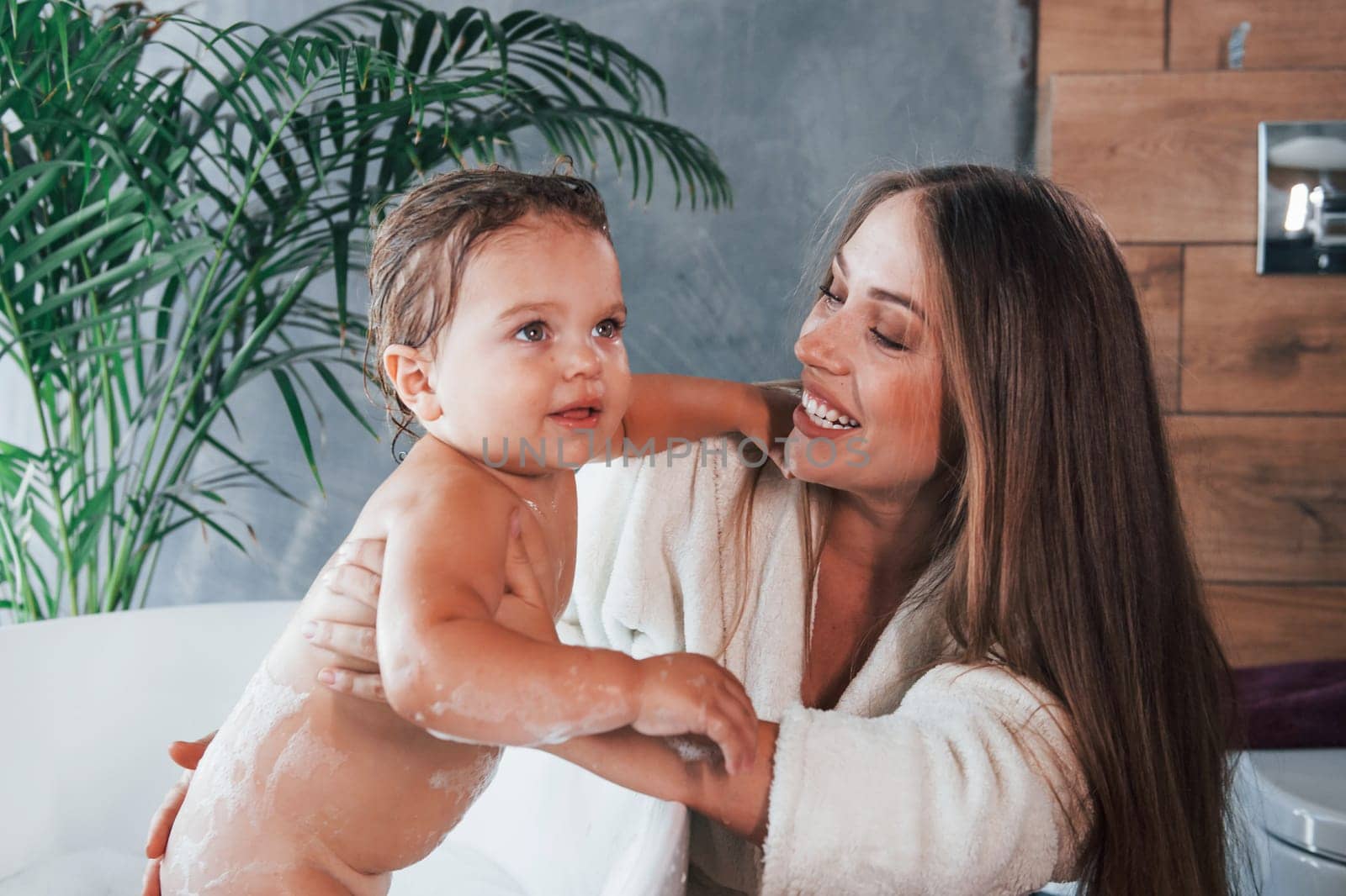 Young mother helps her daughter to wash in the bath by Standret