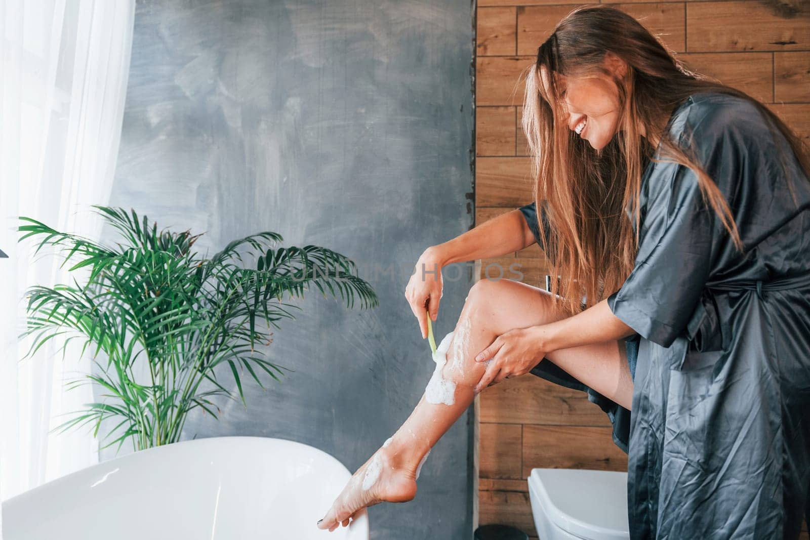 Beautiful young woman have free time at home in the bath. Shaves legs.