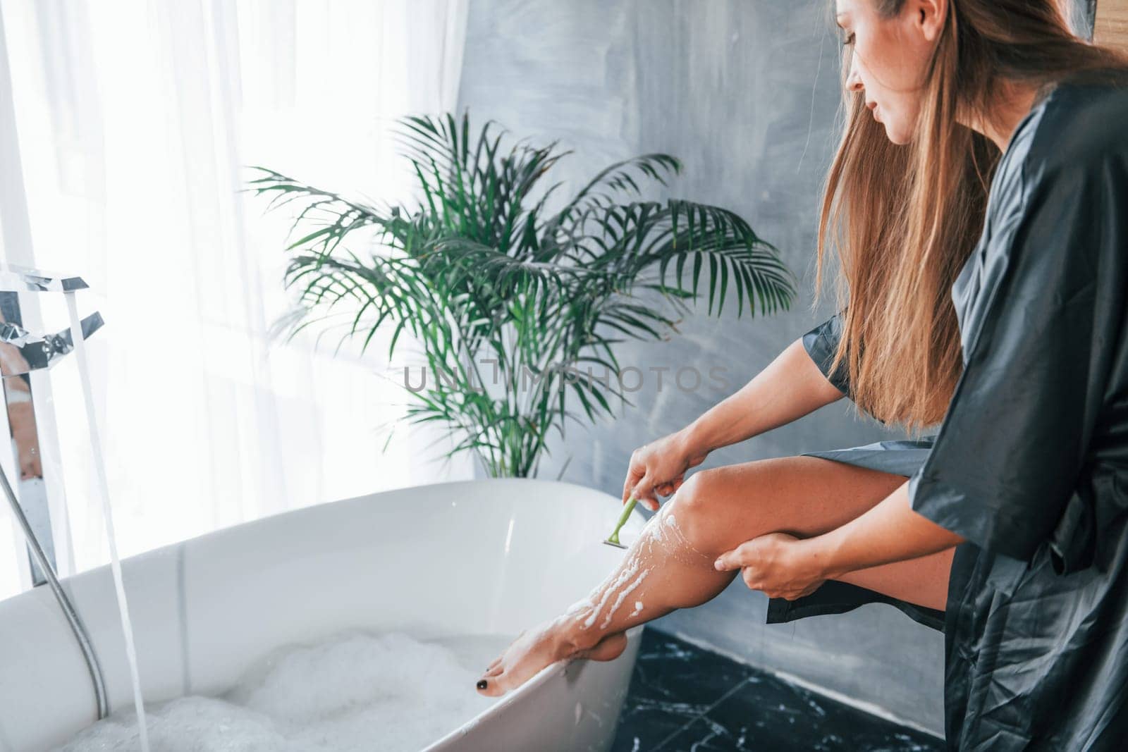 Beautiful young woman have free time at home in the bath. Shaves legs.
