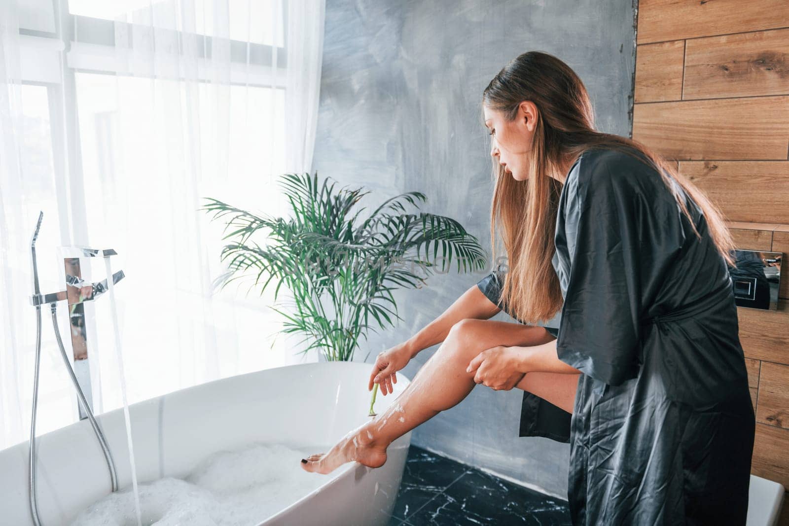 Beautiful young woman have free time at home in the bath. Shaves legs.