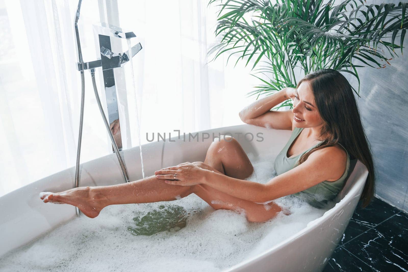 Uses phone. Beautiful young woman have free time at home in the bath.