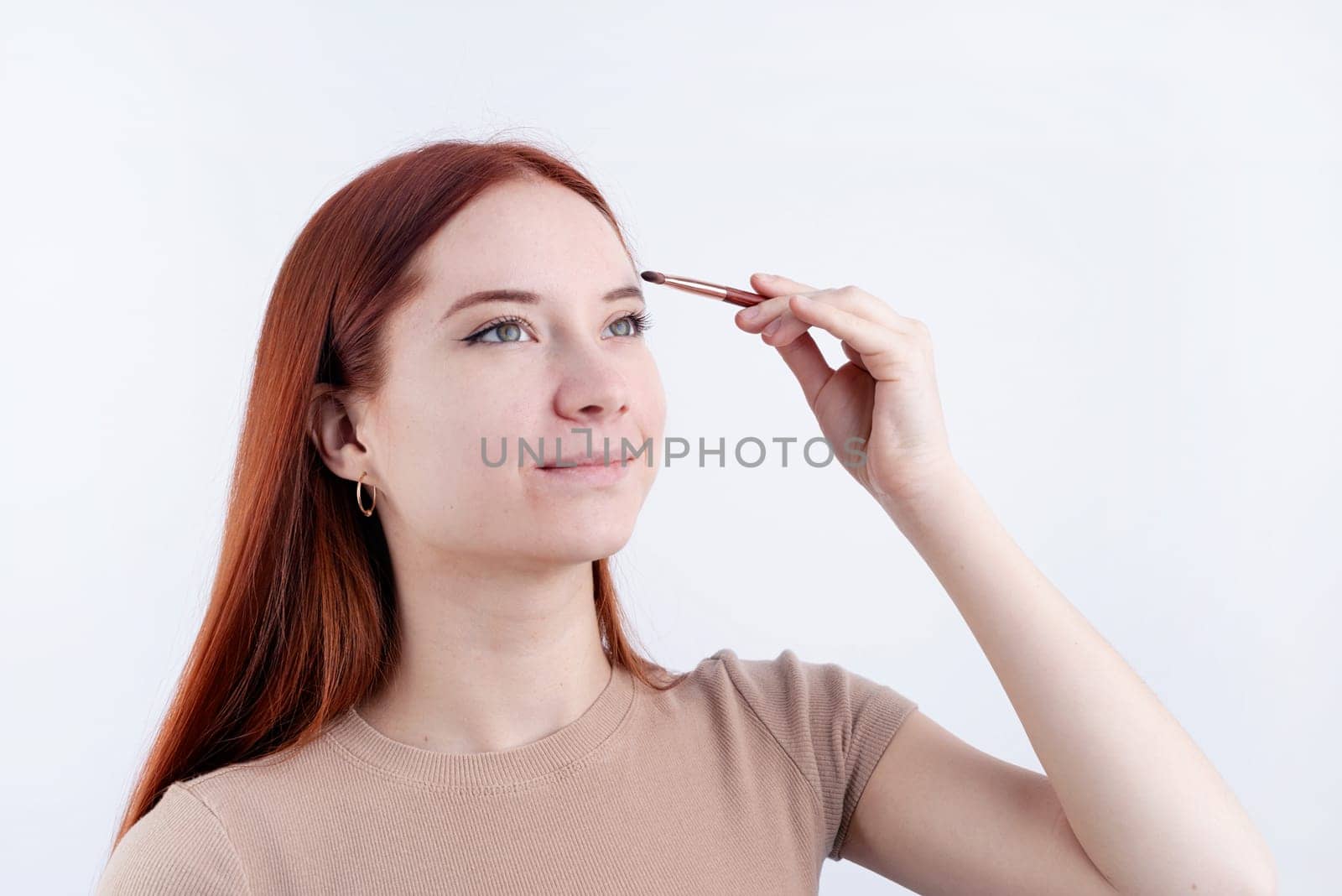 Joyful redhead young woman using makeup brush making up isolated on white background by Desperada