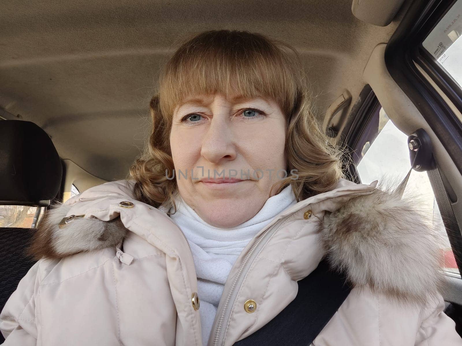 Woman sitting in the car in road trip. Blonde senior Woman driving transport. Lady travelling in cold time