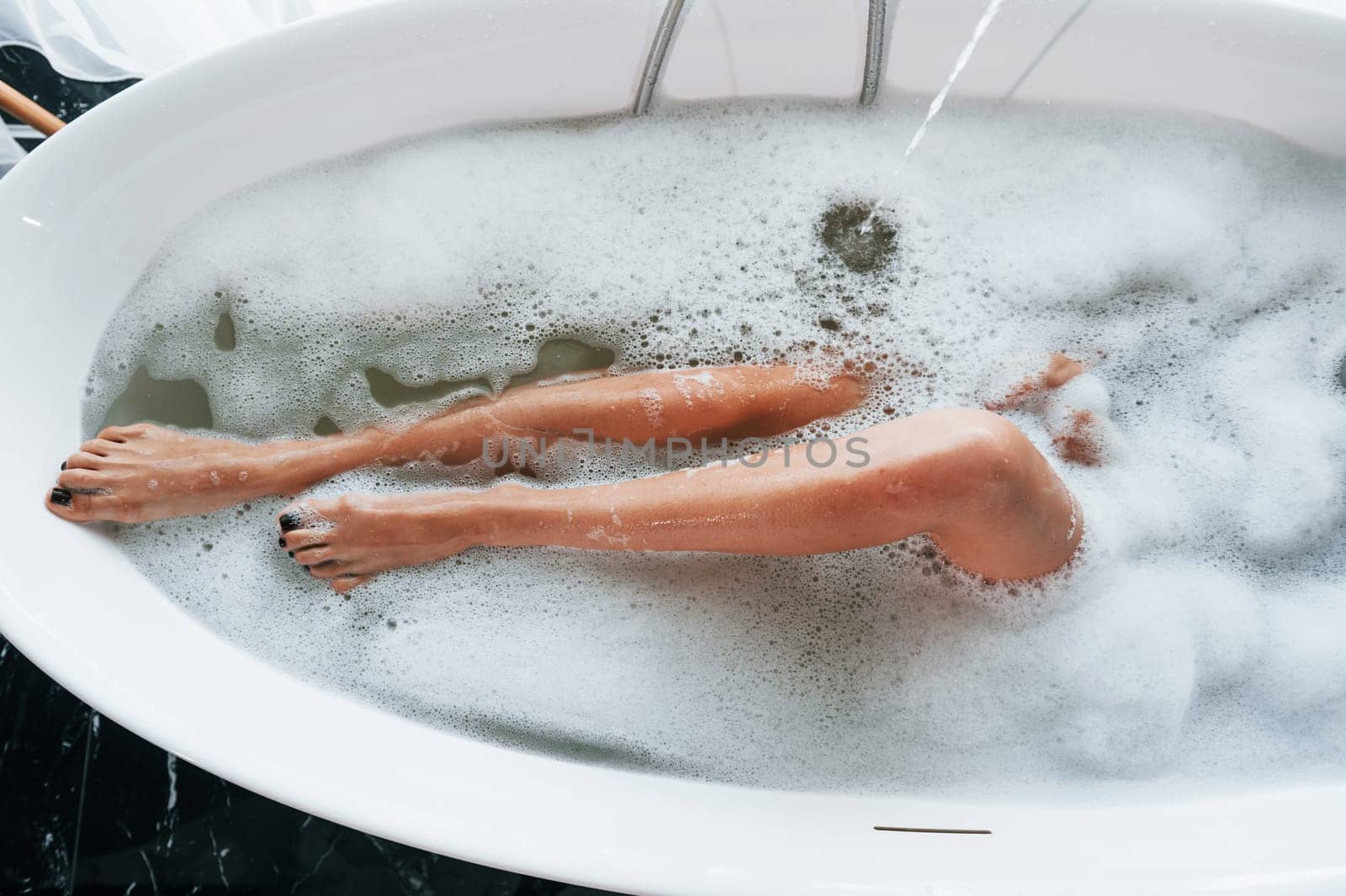 Particle view of legs. Beautiful young woman have free time at home in the bath.