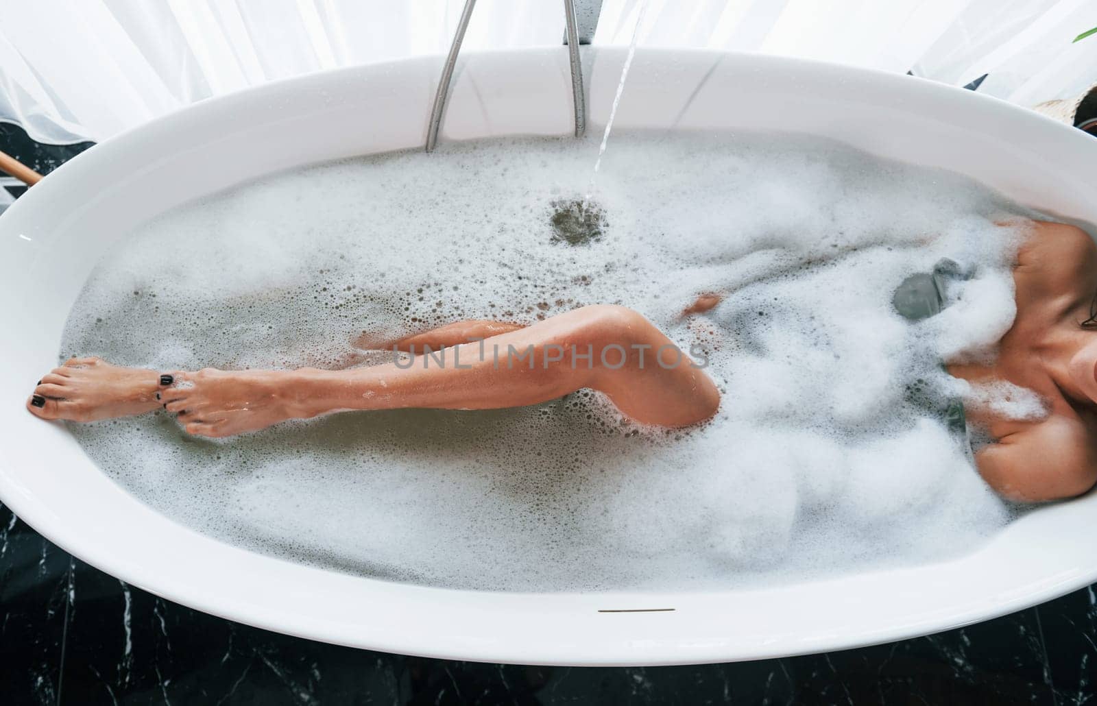 Particle view of legs. Beautiful young woman have free time at home in the bath.