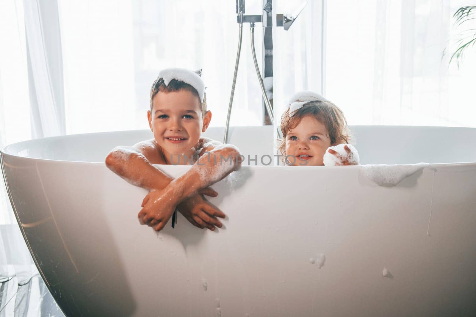 Two kids having fun and washing themselves in the bath at home. Posing for a camera by Standret