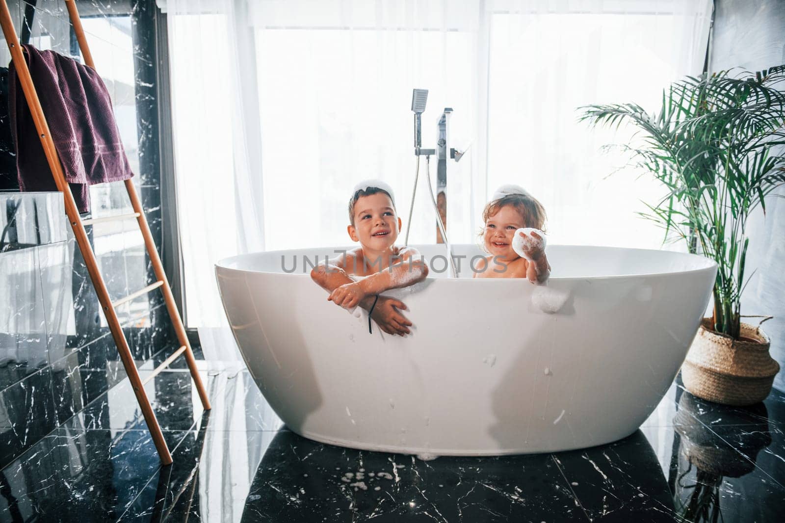 Two kids having fun and washing themselves in the bath at home. Posing for a camera by Standret