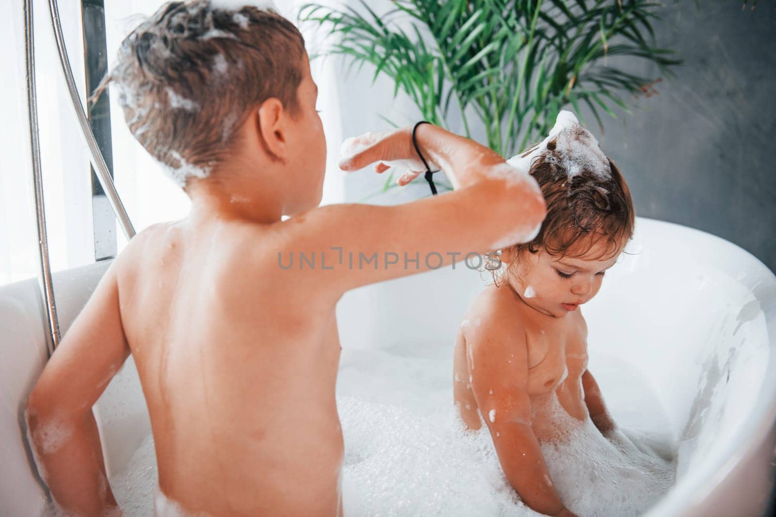 Two kids having fun and washing themselves in the bath at home by Standret