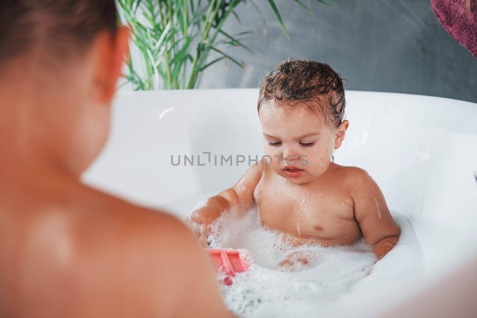 Two kids having fun and washing themselves in the bath at home.