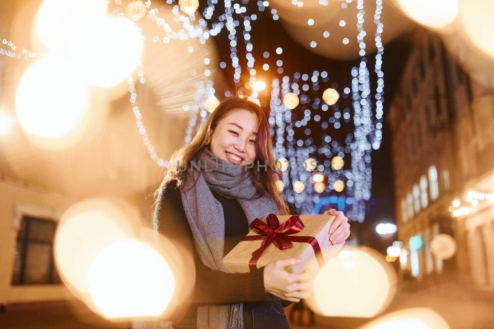 With gift box. Cute and happy asian young woman outdoors in the city celebrates New year.