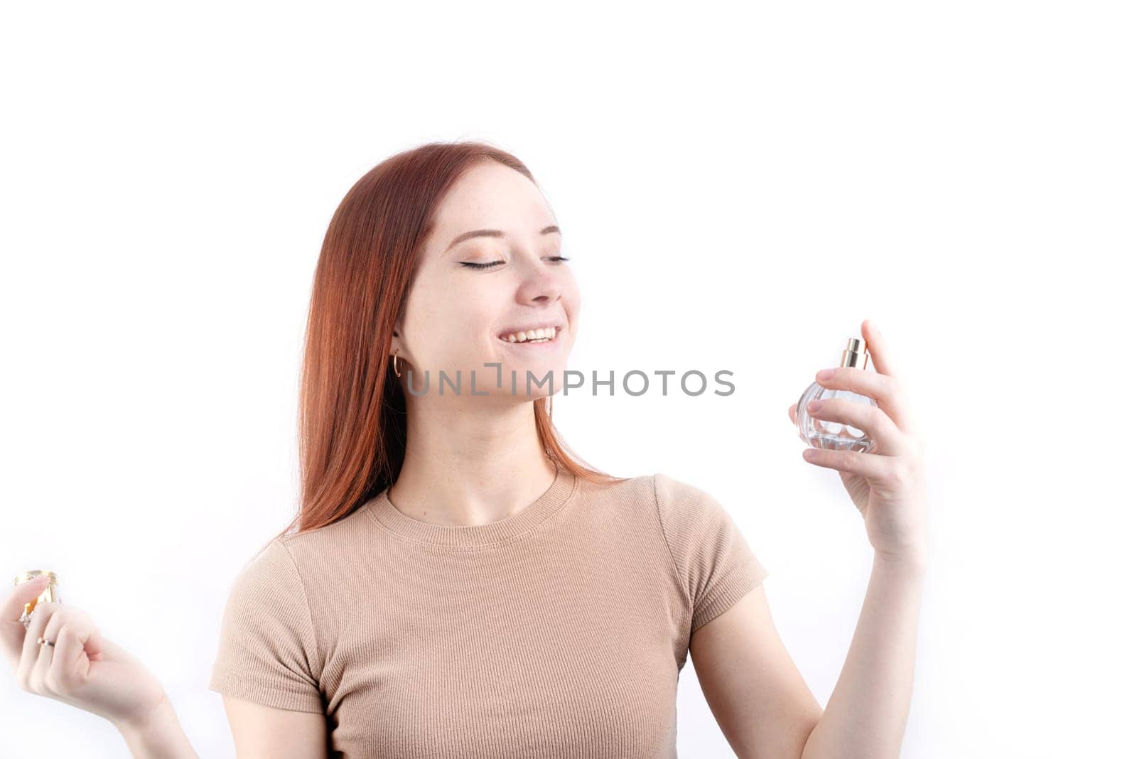 Happy young woman using perfume, holding glass bottle isolated on white background by Desperada