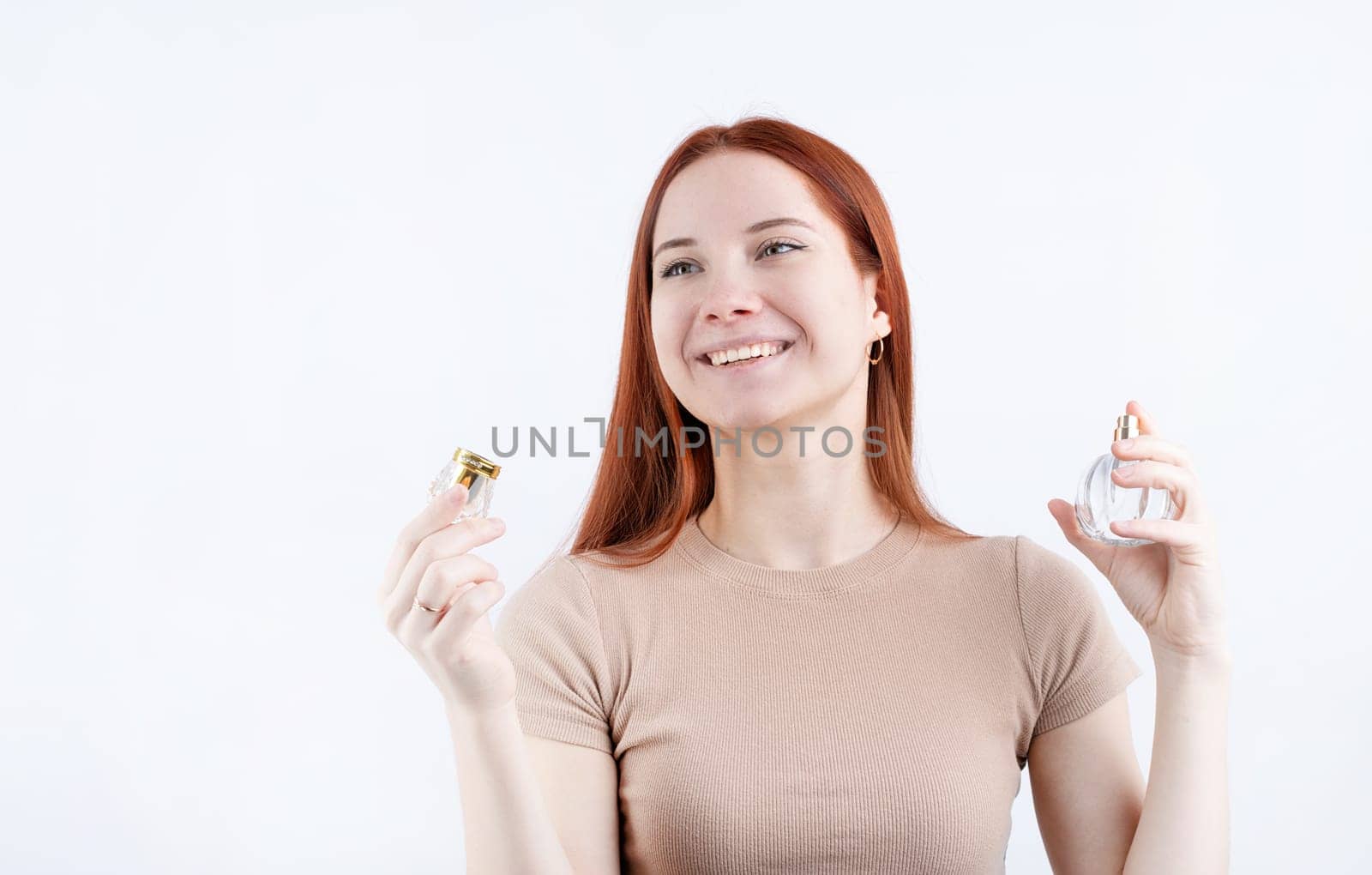 Happy young caucasian woman using perfume, holding glass bottle isolated on white background