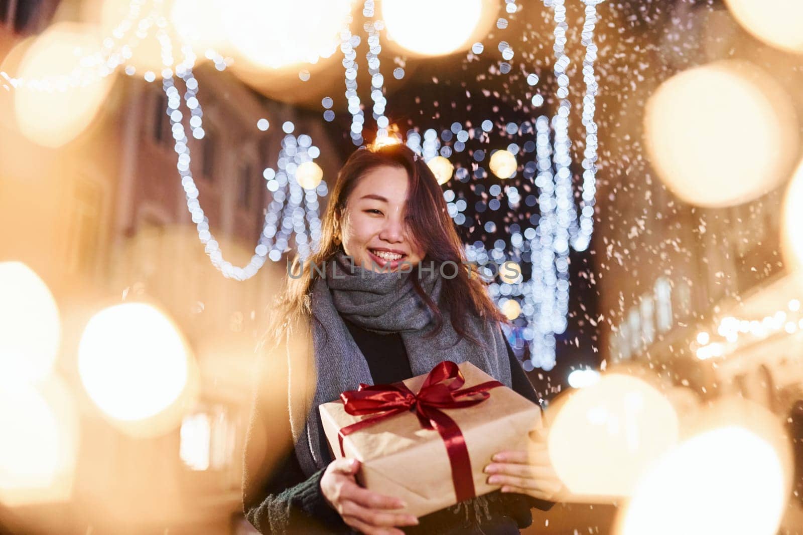With gift box. Cute and happy asian young woman outdoors in the city celebrates New year.