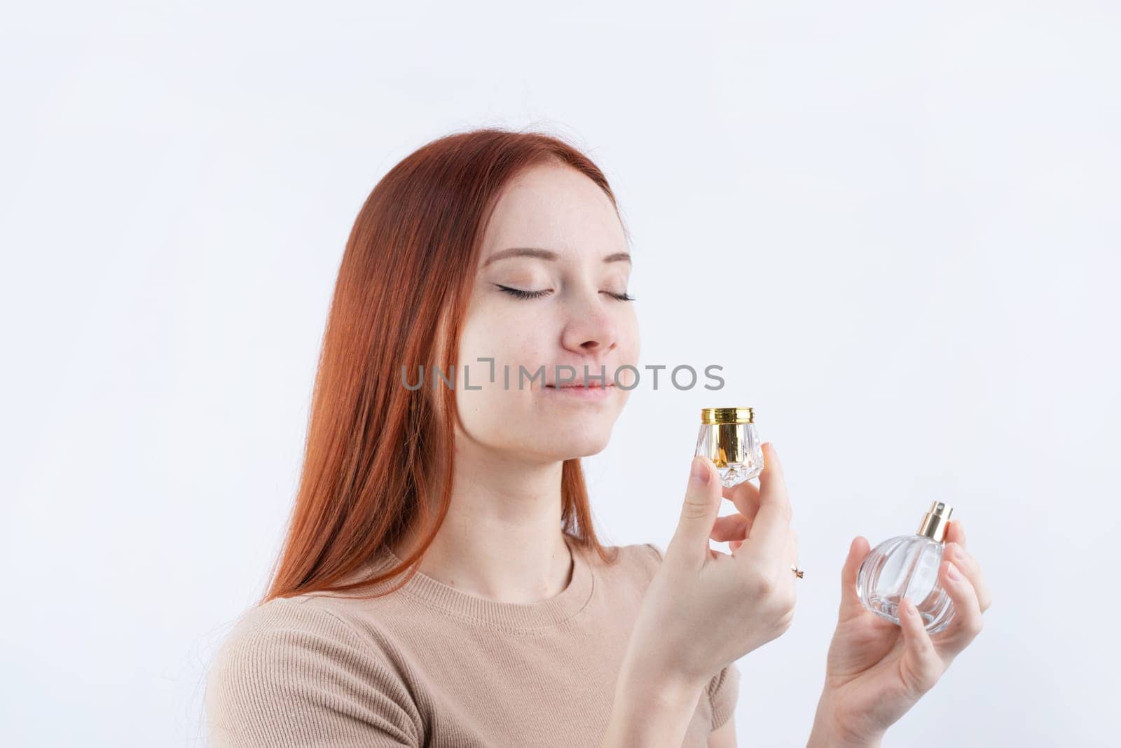 Happy young woman smelling perfume, holding glass bottle isolated on white background by Desperada