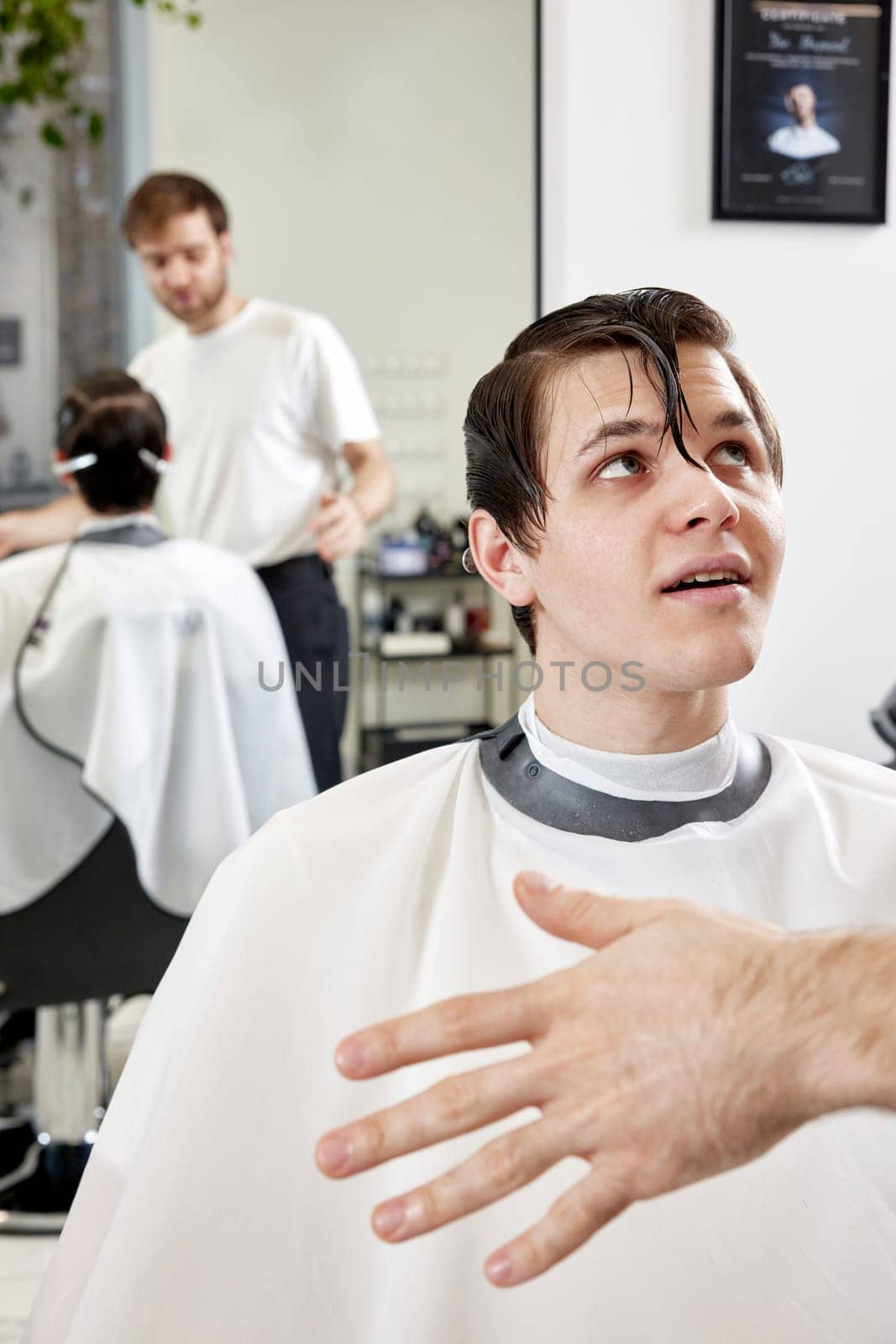 Barber talking to young client man before haircut at barbershop. client tells what haircut he wants
