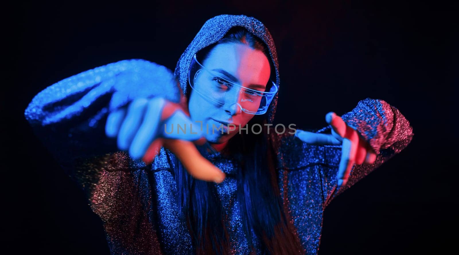 Does gestures by hands. Portrait of young girl that is in eyeglasses in blue neon lighting.