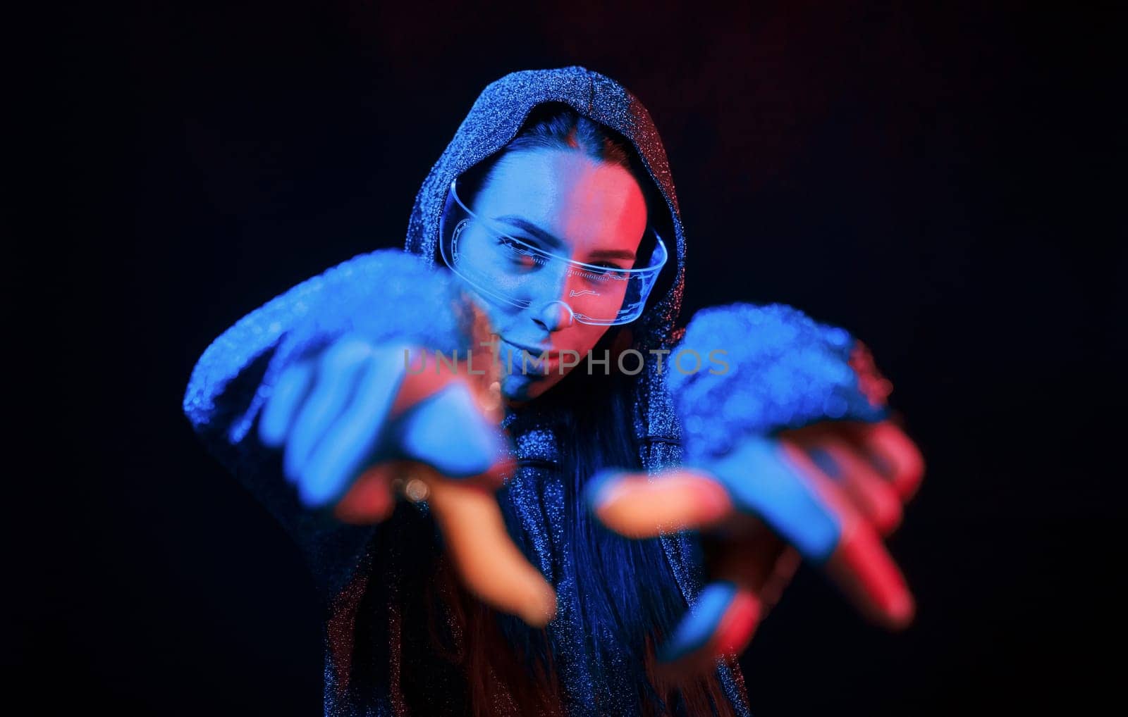 Does gestures by hands. Portrait of young girl that is in eyeglasses in blue neon lighting.