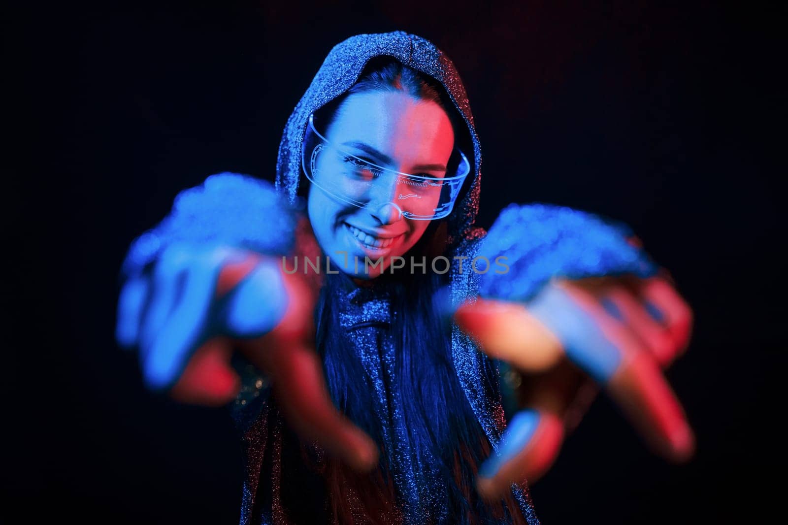 Does gestures by hands. Portrait of young girl that is in eyeglasses in blue neon lighting.