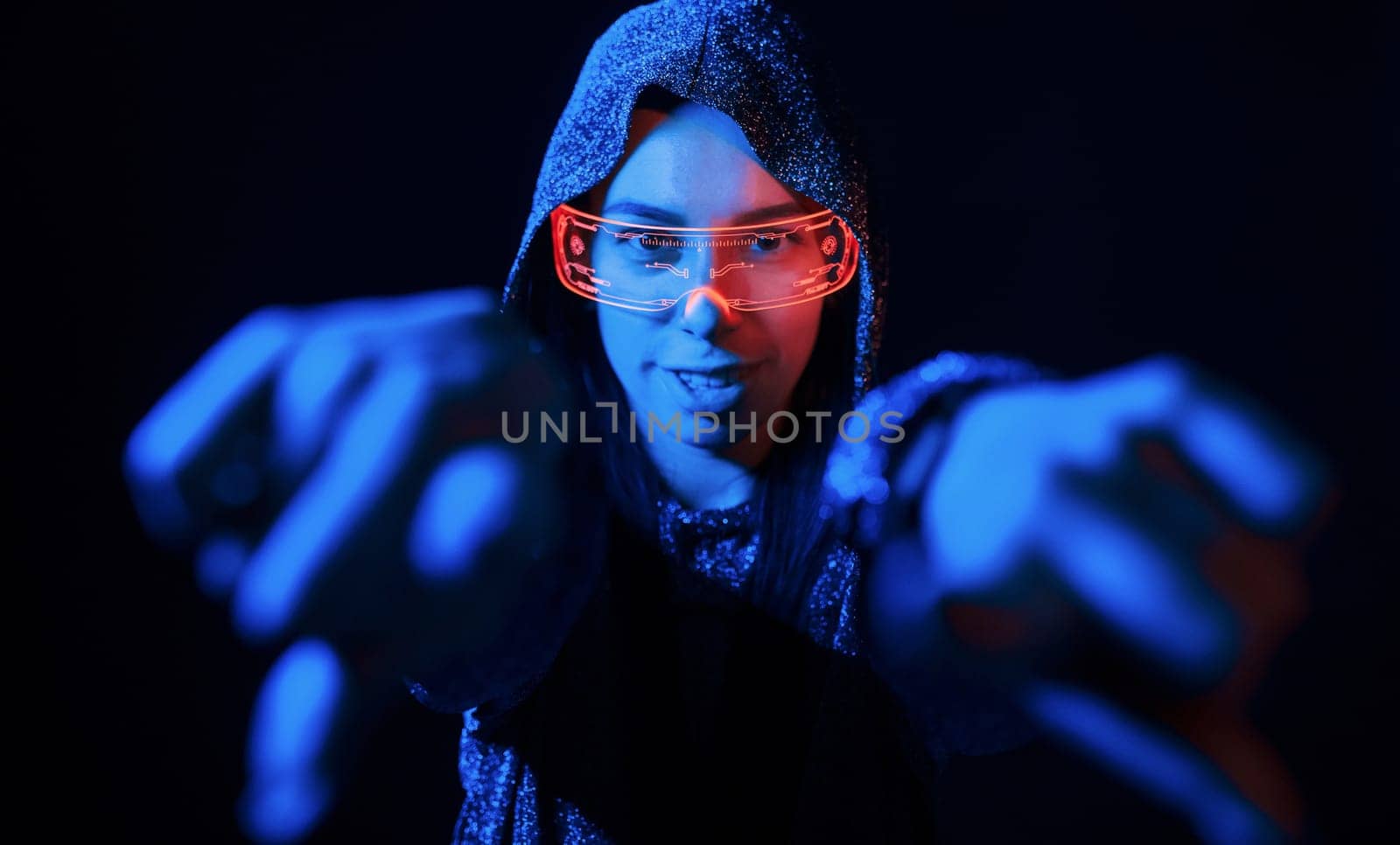 Does gestures by hands. Portrait of young girl that is in eyeglasses in blue neon lighting.