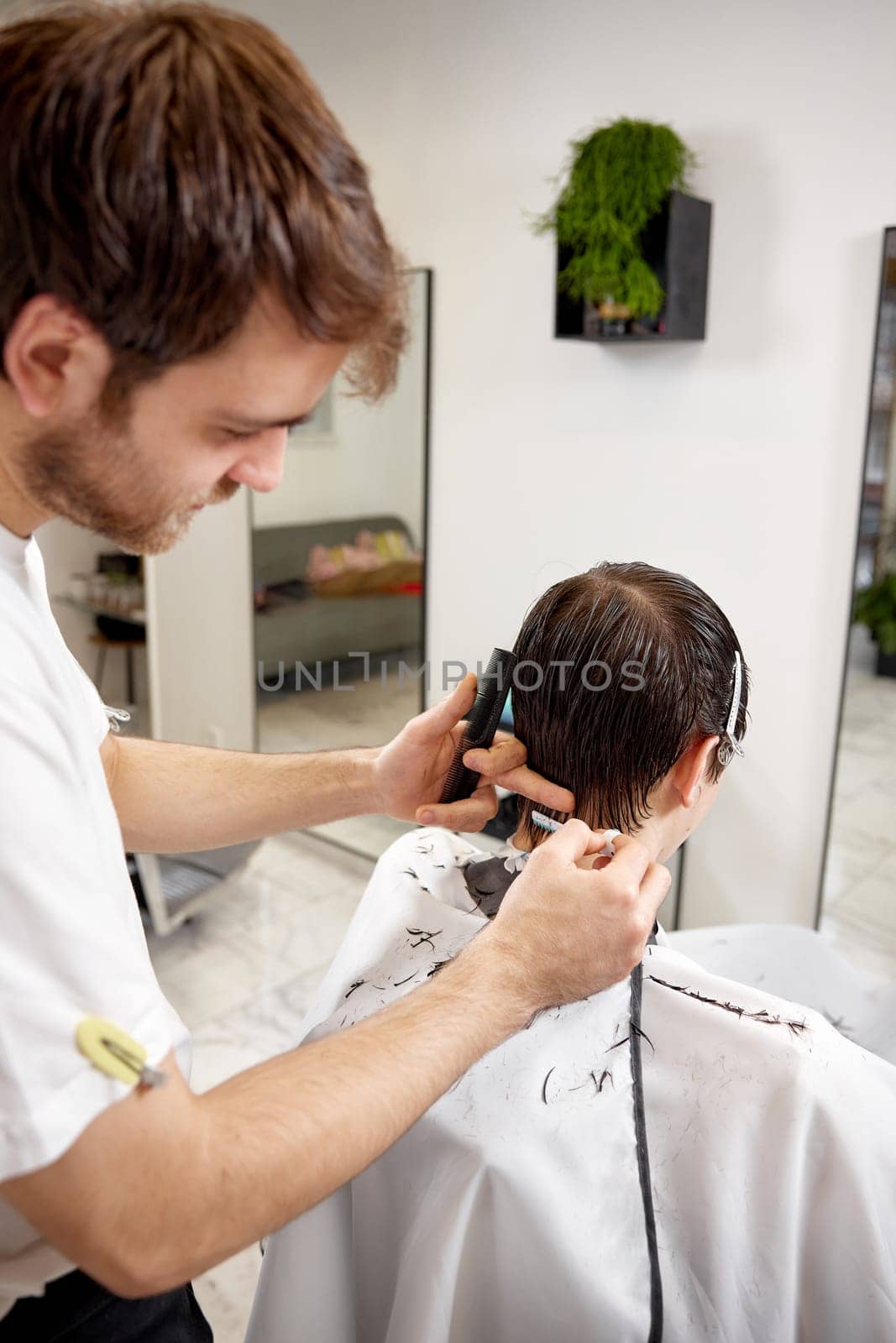 young caucasian man getting haircut by professional male hairstylist using comb and grooming scissors at barber shop.