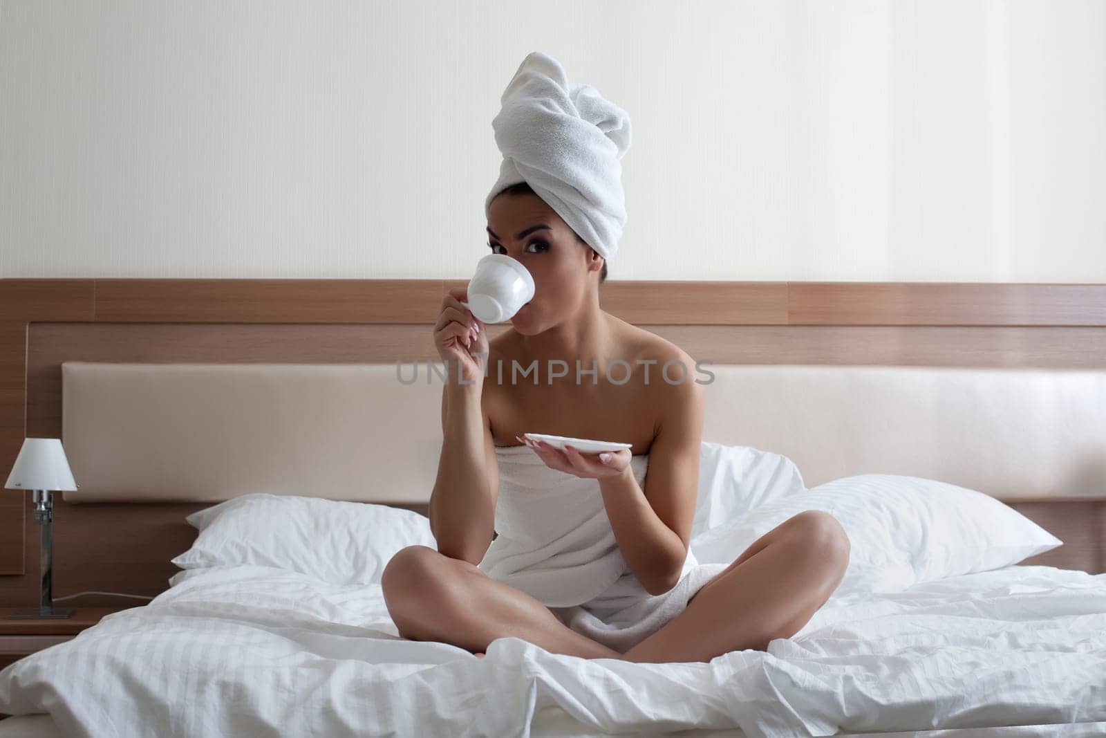 Full length portrait of young woman drinking coffee in bed
