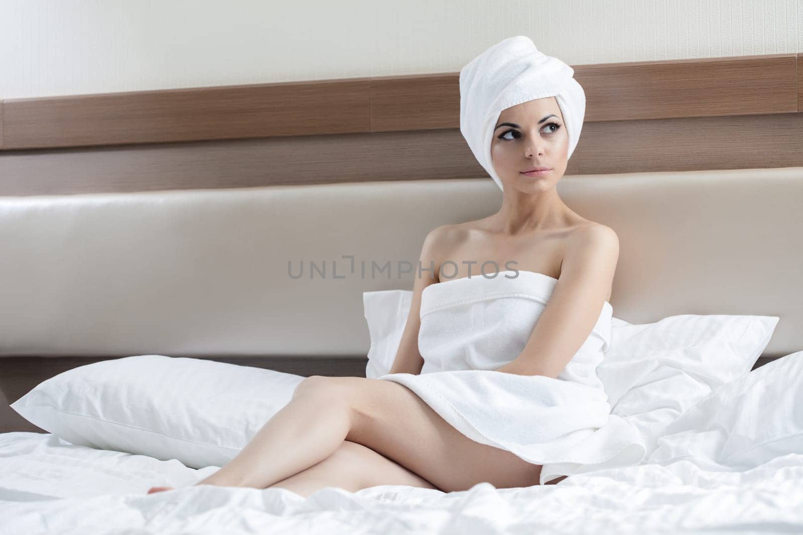 Portrait of Sexy woman sitting on bed after bath in hotel room with towel on head