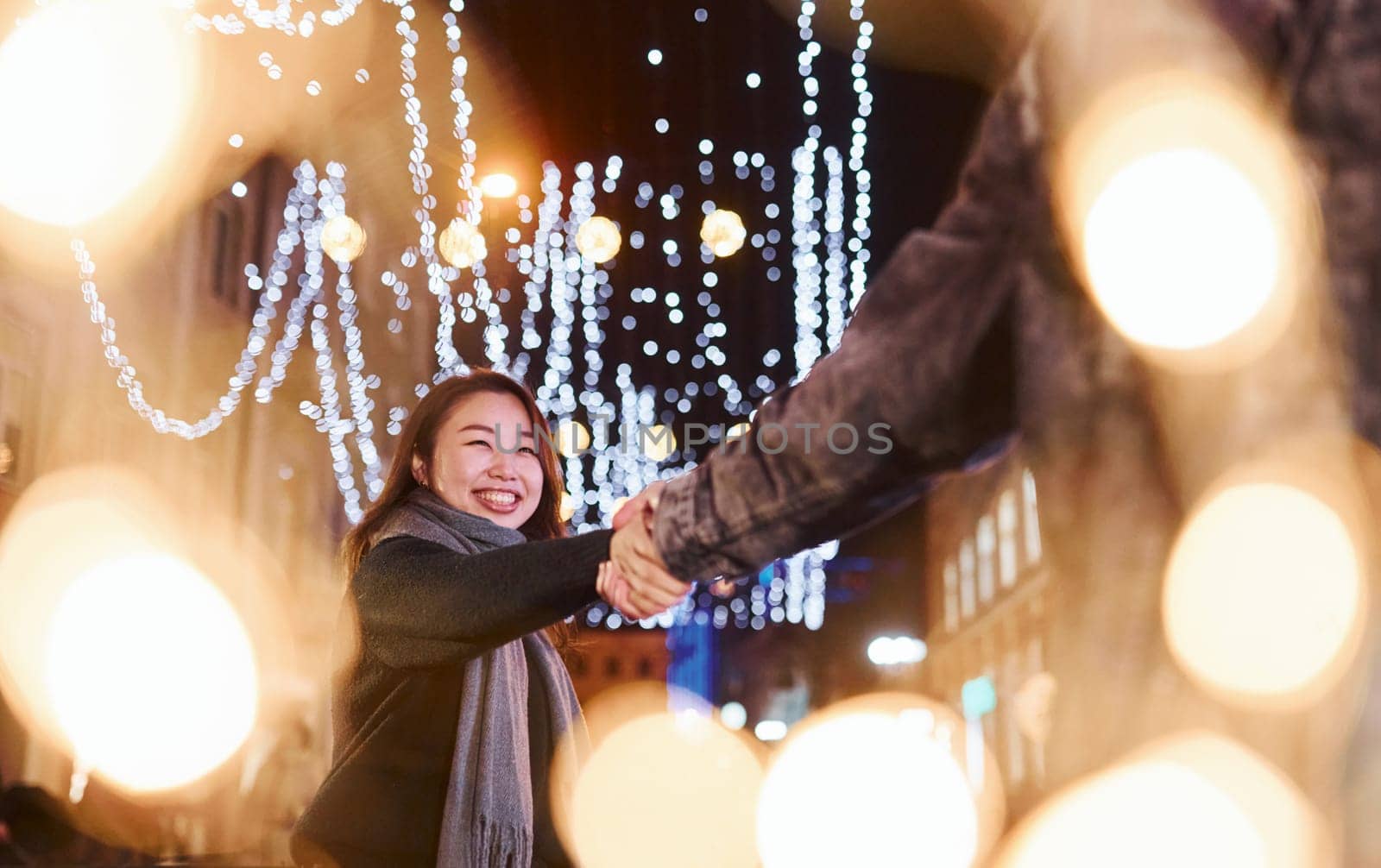 Artificial lighting by garlands. Happy multiracial couple together outdoors in the city celebrating New year.