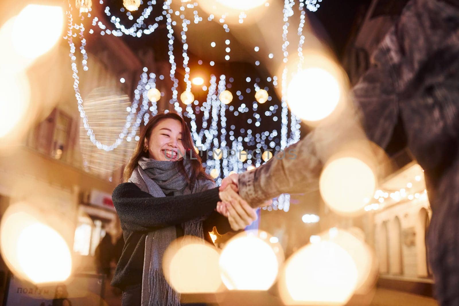 Artificial lighting by garlands. Happy multiracial couple together outdoors in the city celebrating New year.