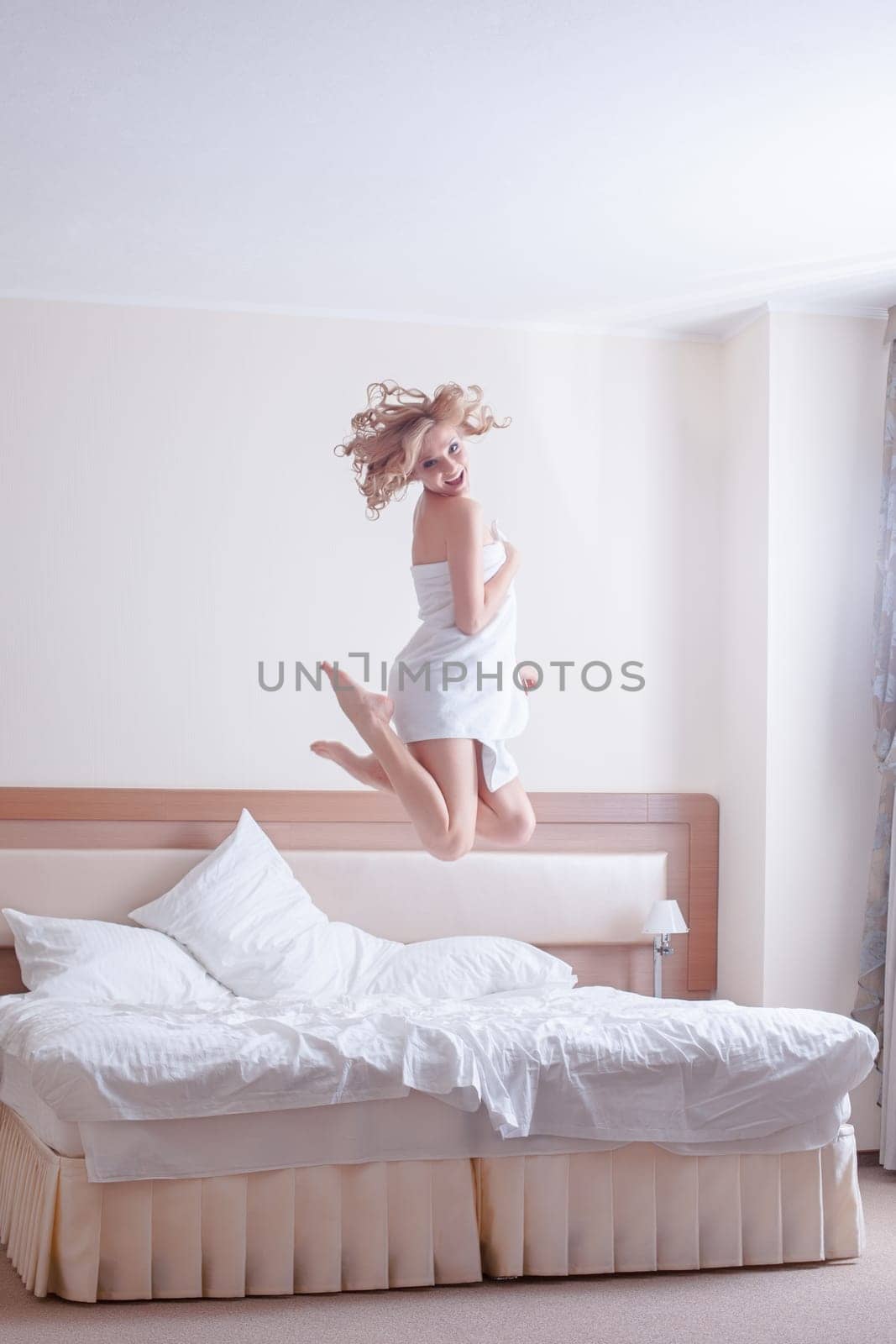 Full length portrait of happy young woman jumping on bed