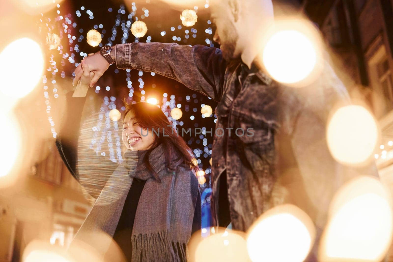 Artificial lighting by garlands. Happy multiracial couple together outdoors in the city celebrating New year.