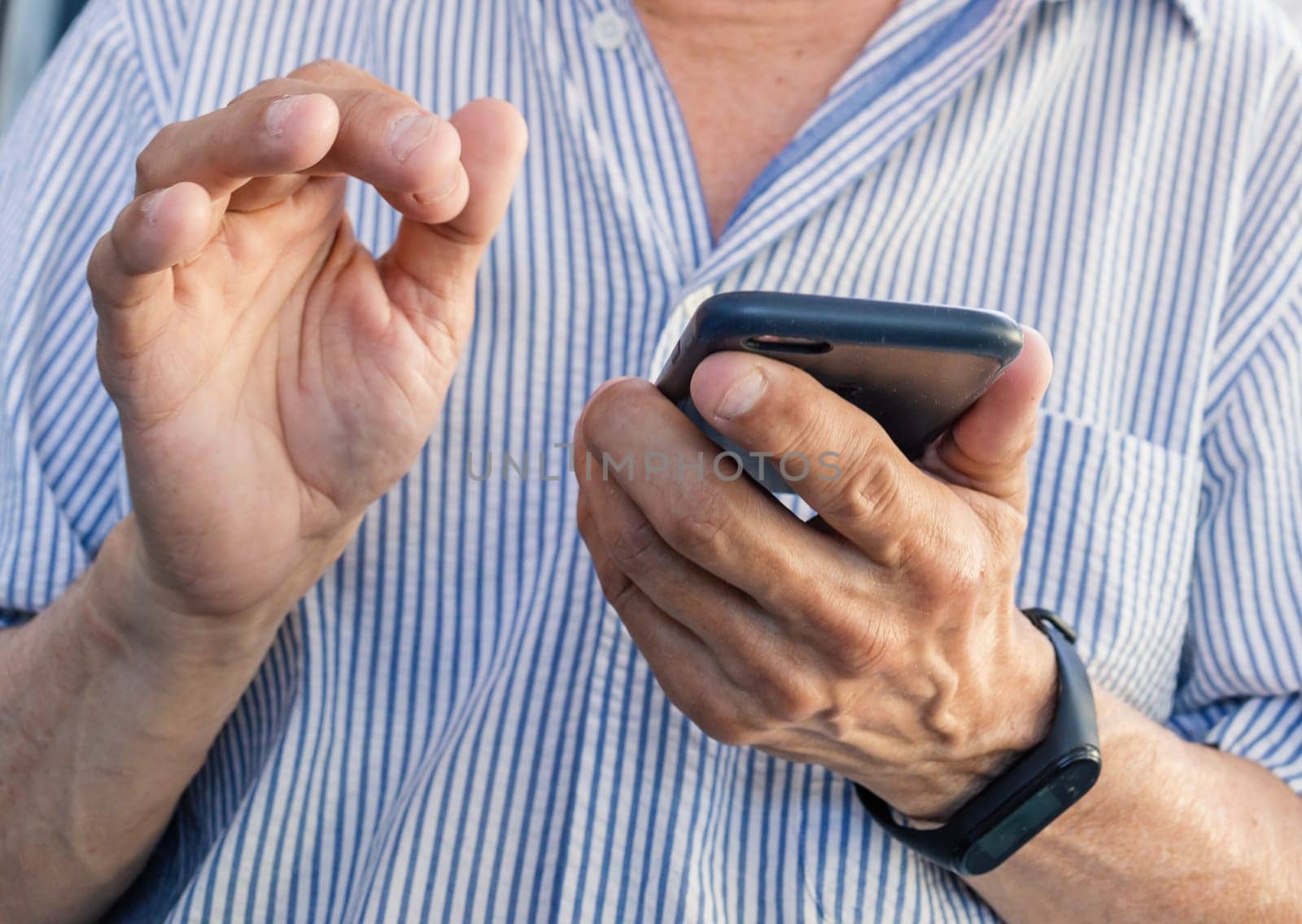 An elderly man holds a mobile phone in his hands with nibbled nails. Close-up image of an elderly man's hands