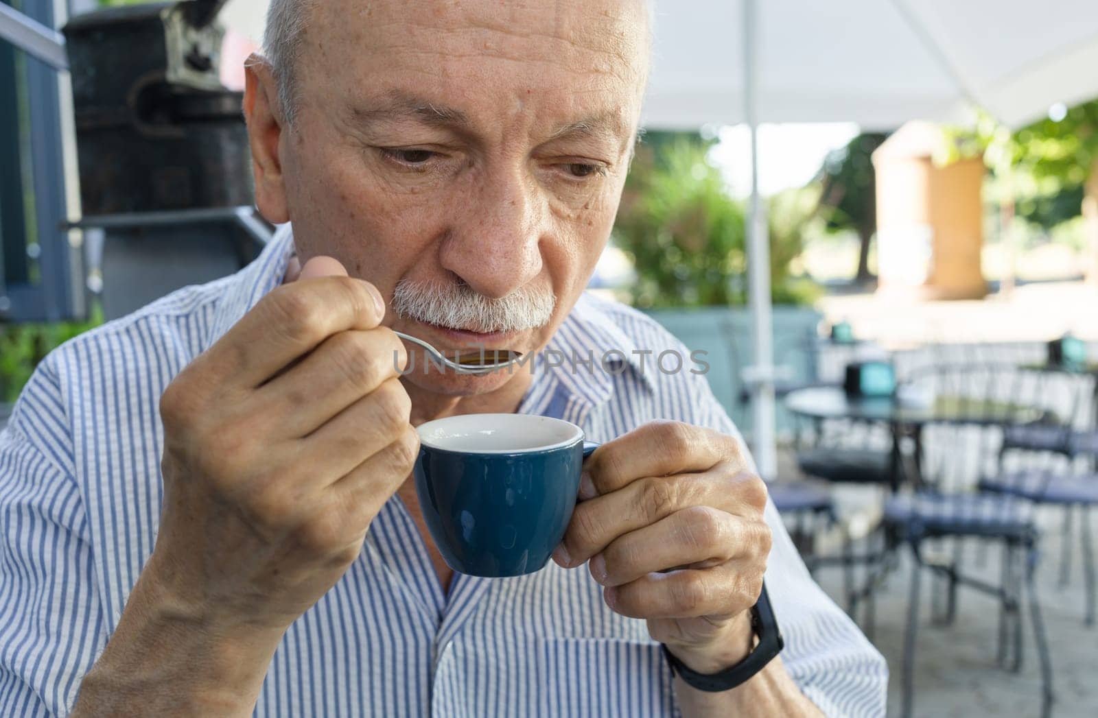Elderly man drinking espresso coffee at an outdoor cafe by palinchak