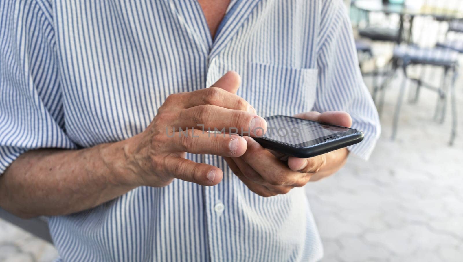 An elderly man holds a mobile phone in his hands with nibbled nails. Close-up image of an elderly man's hands