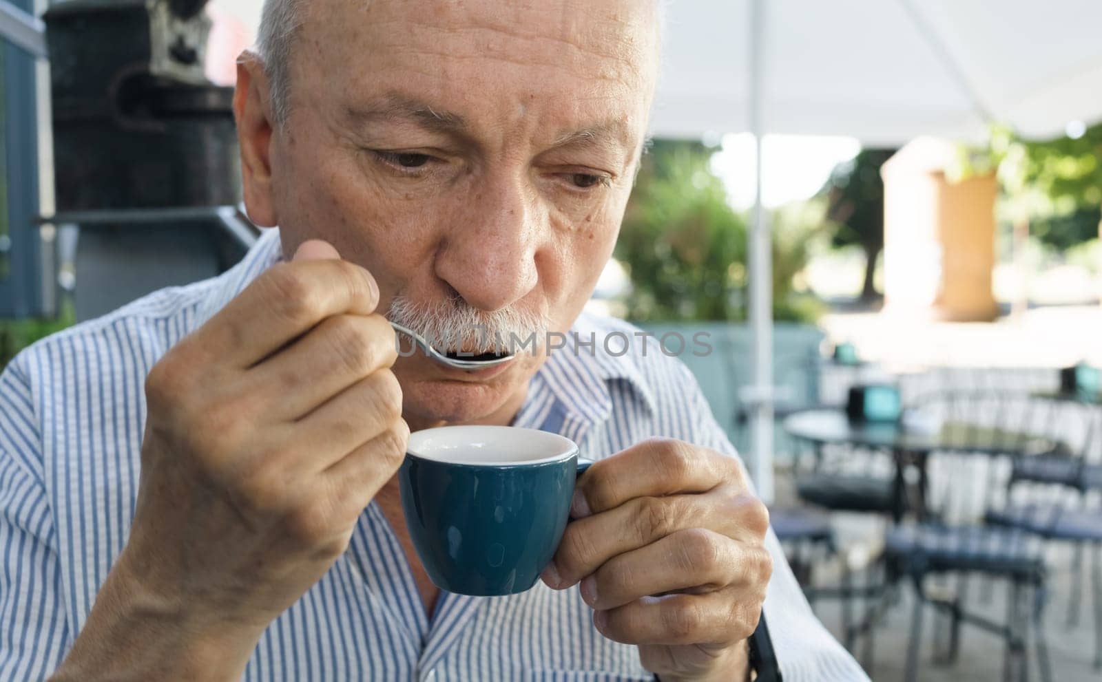 Lifestyle concept. An elderly man drinking espresso coffee at an outdoor cafe in the early hours of the morning before work.
