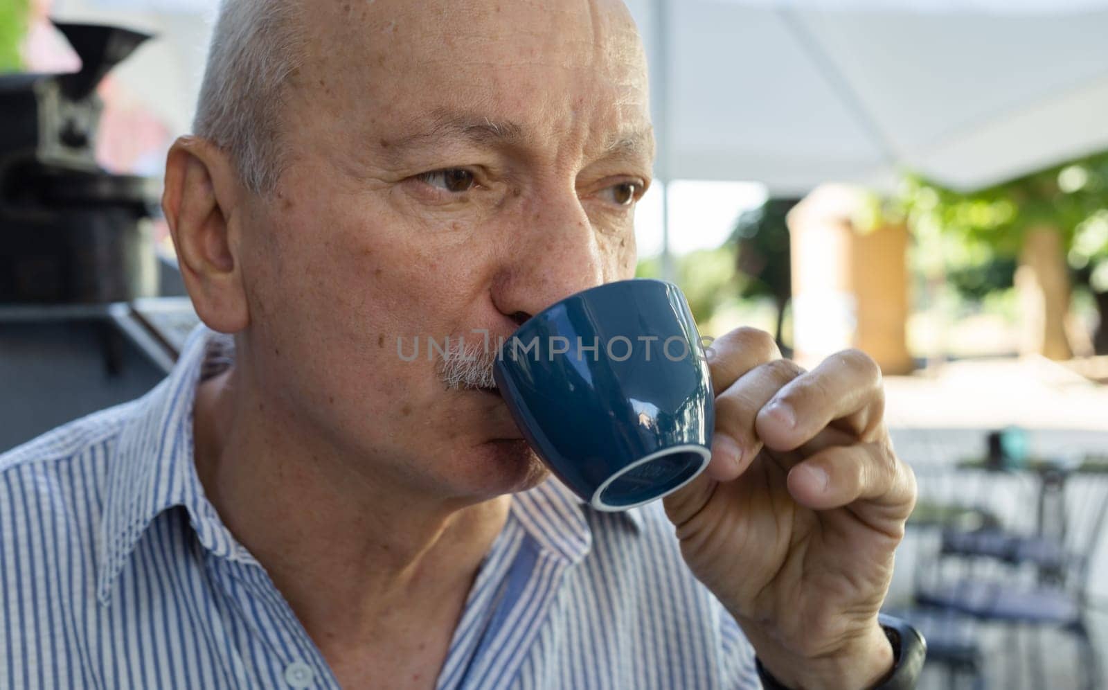 Elderly man drinking espresso coffee at an outdoor cafe by palinchak