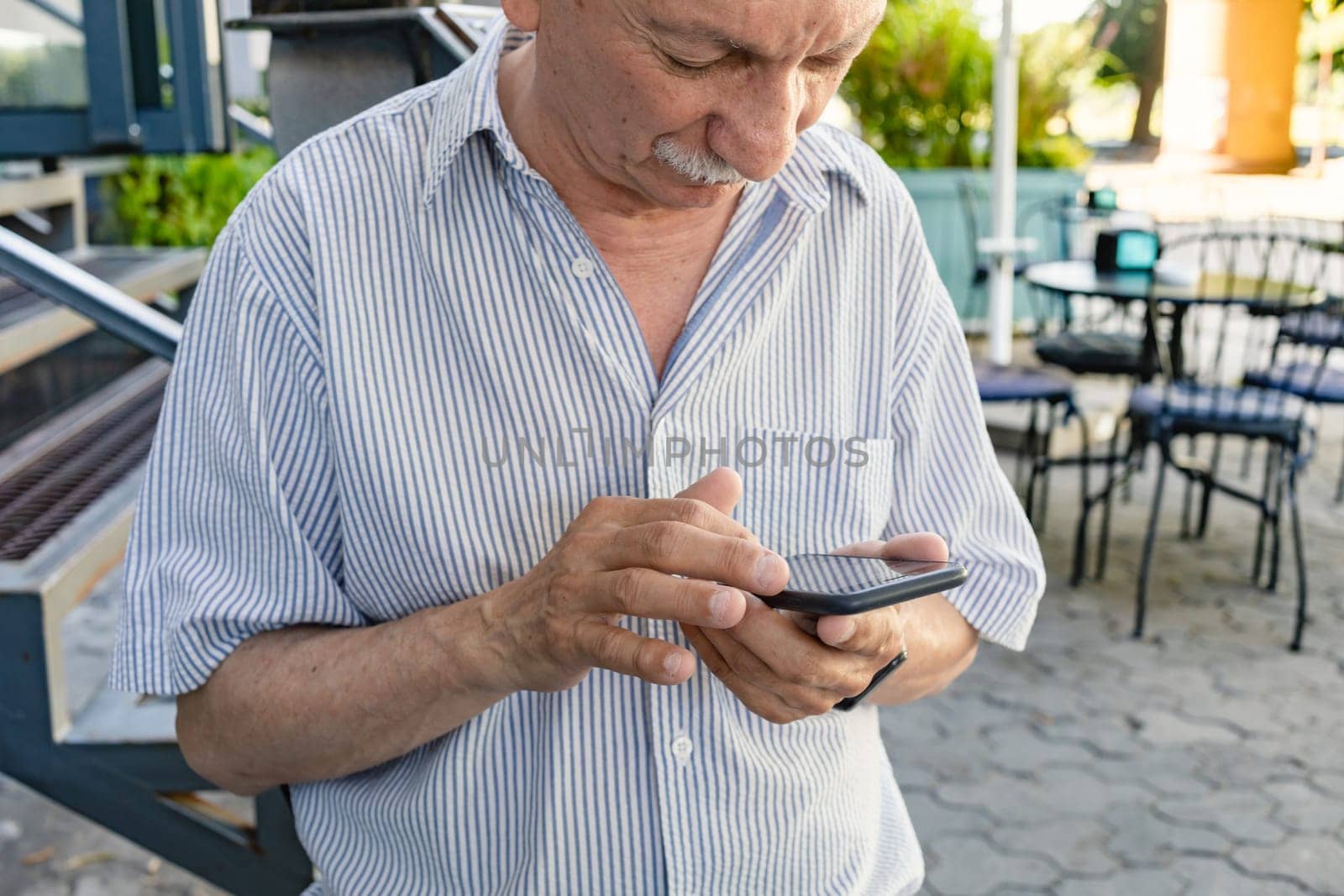 Elderly man is holding a mobile phone in his hands by palinchak