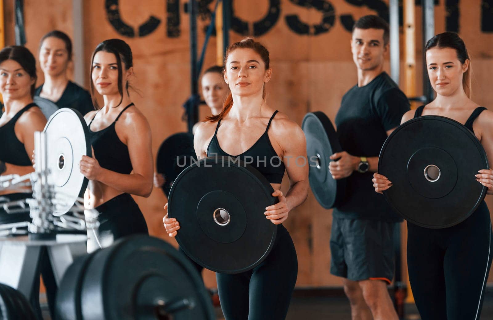 Holding weights. Group of young sportive people have crossfit day indoors in gym.