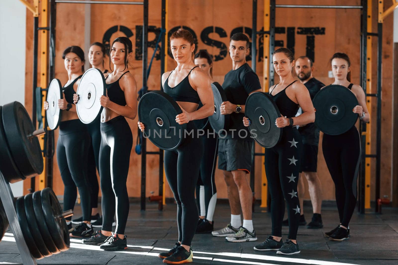 Holding weights. Group of young sportive people have crossfit day indoors in gym.