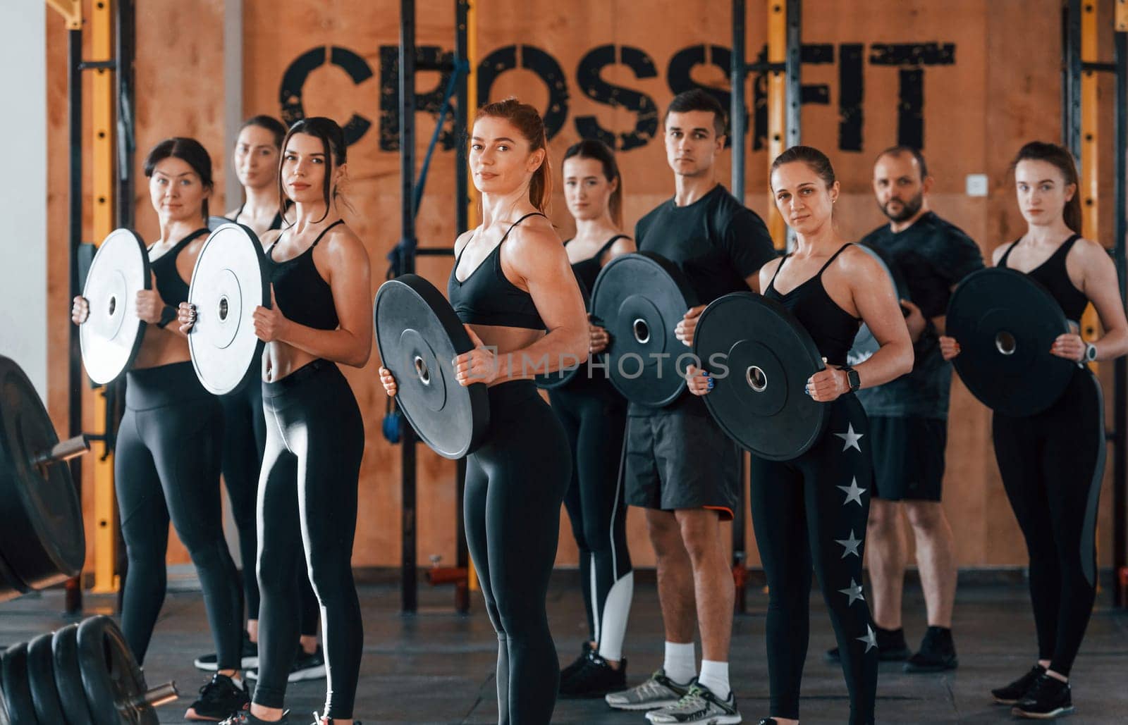 Holding weights. Group of young sportive people have crossfit day indoors in gym.