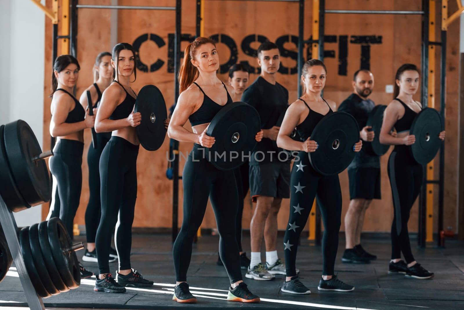 Holding weights. Group of young sportive people have crossfit day indoors in gym.