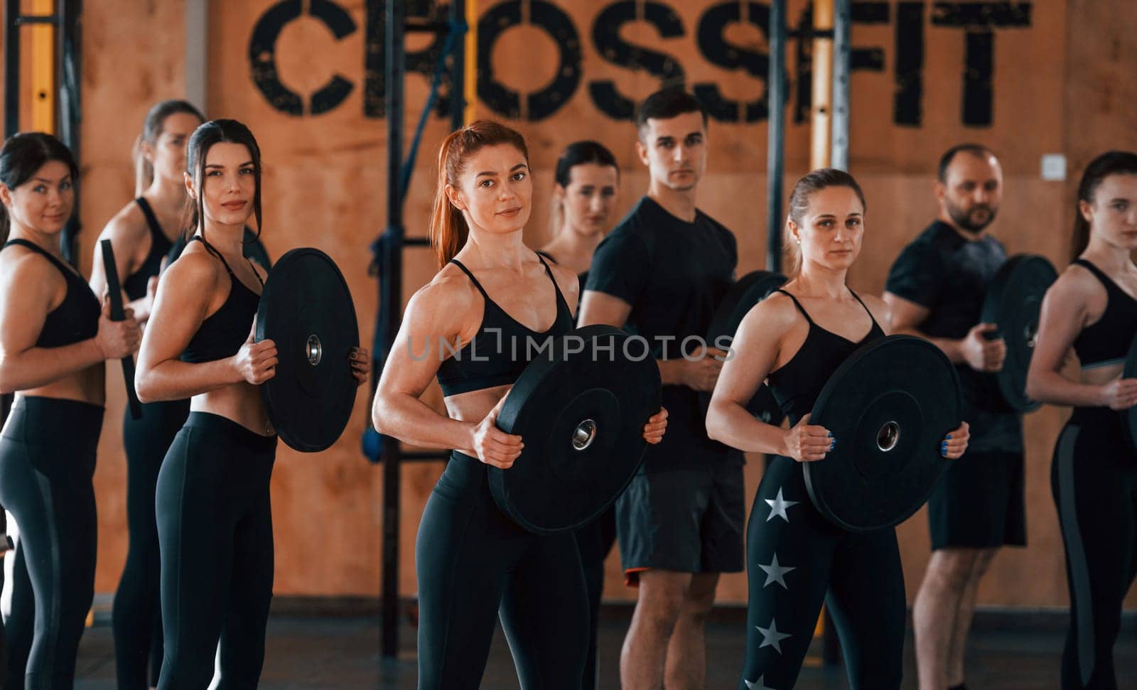 Holding weights. Group of young sportive people have crossfit day indoors in gym.