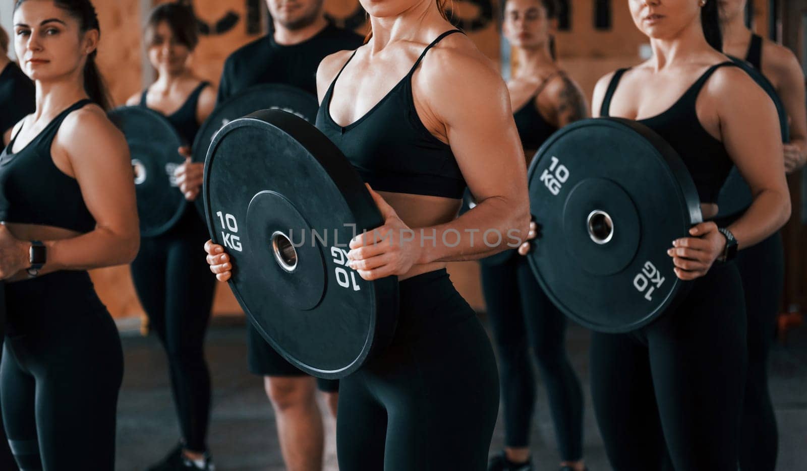Holding weights. Group of young sportive people have crossfit day indoors in gym.