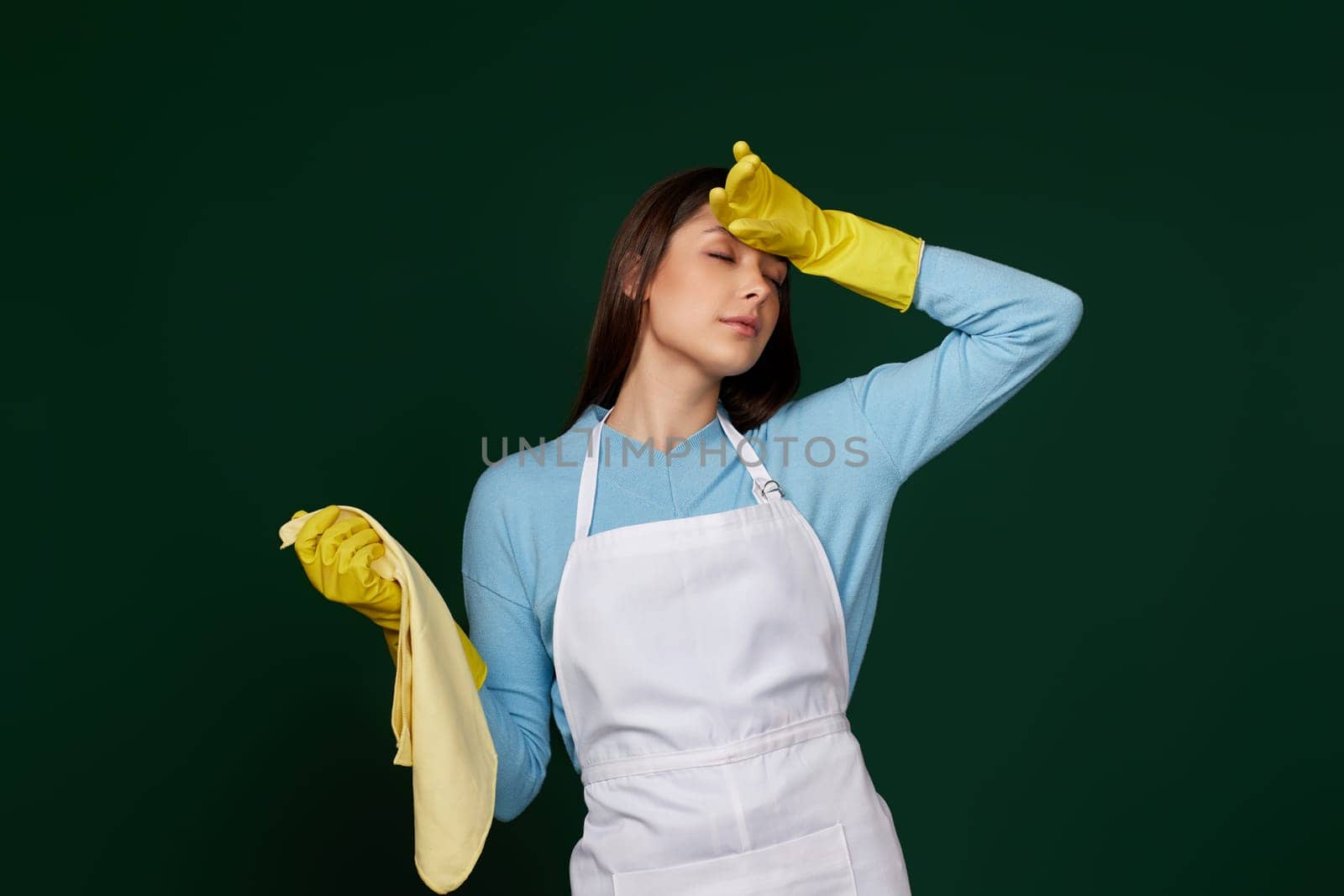 tired woman in yellow gloves and cleaner apron on green background