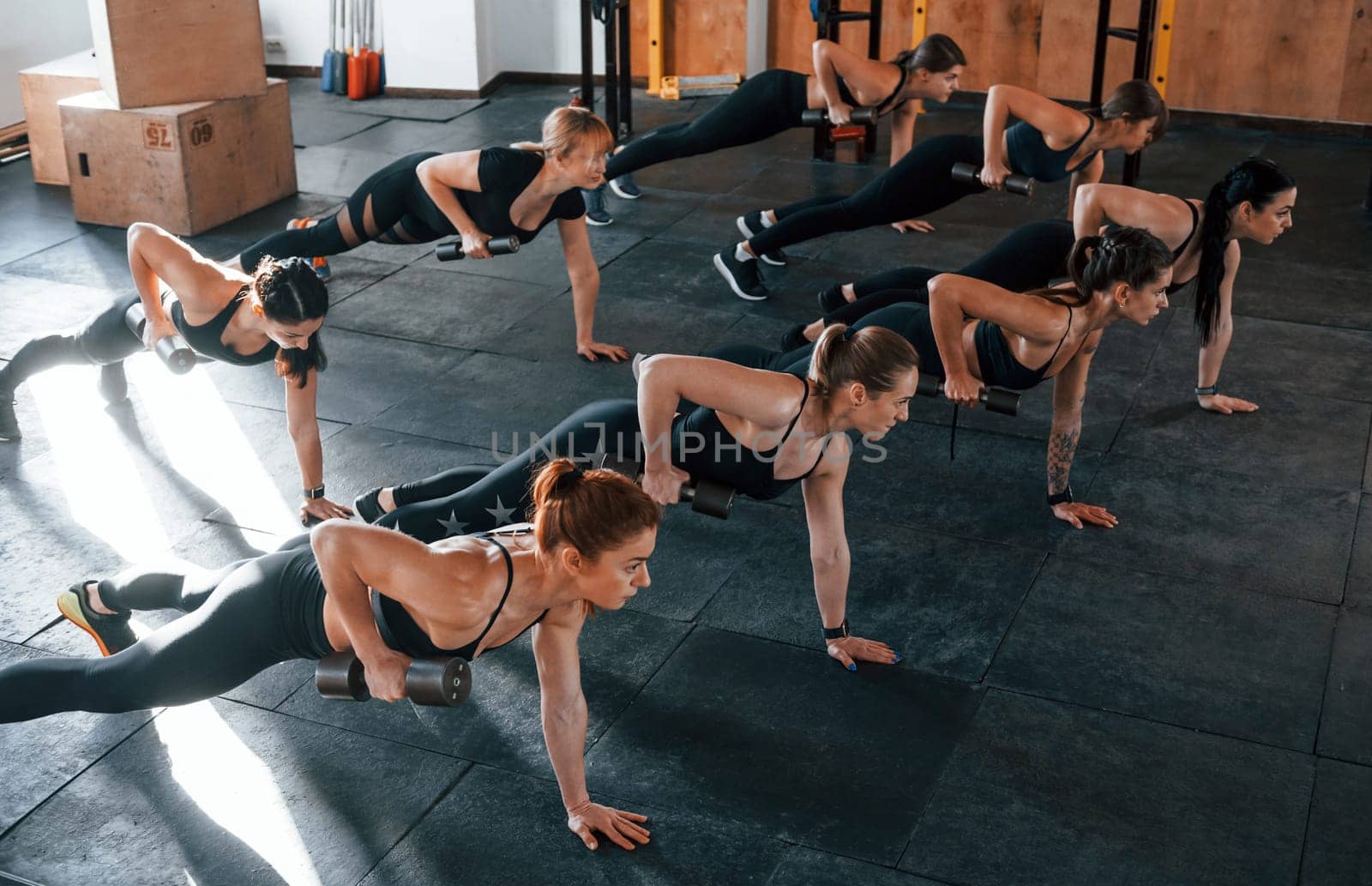 Using barbells. Group of young sportive people have crossfit day indoors in gym.
