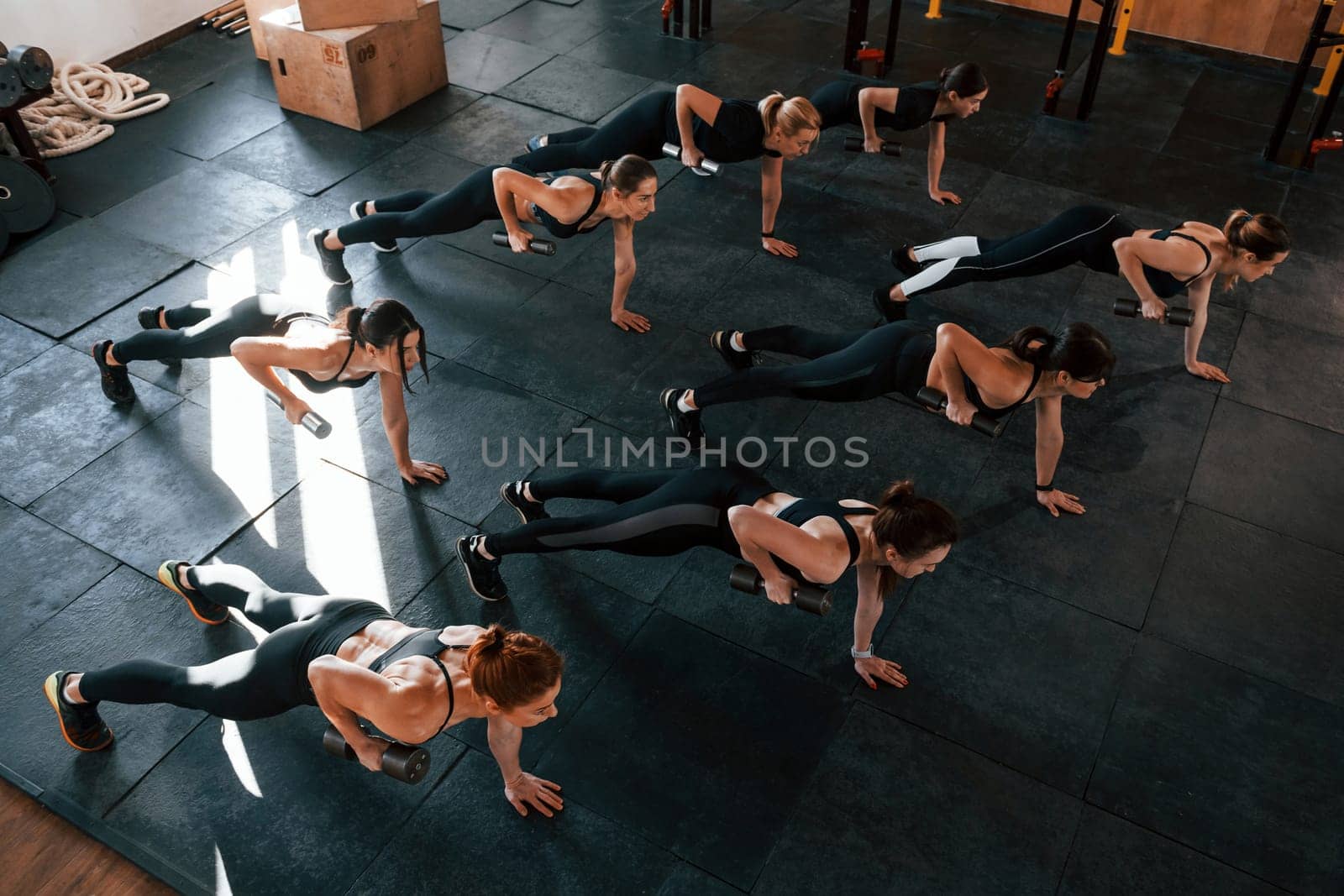 Using barbells. Group of young sportive people have crossfit day indoors in gym.