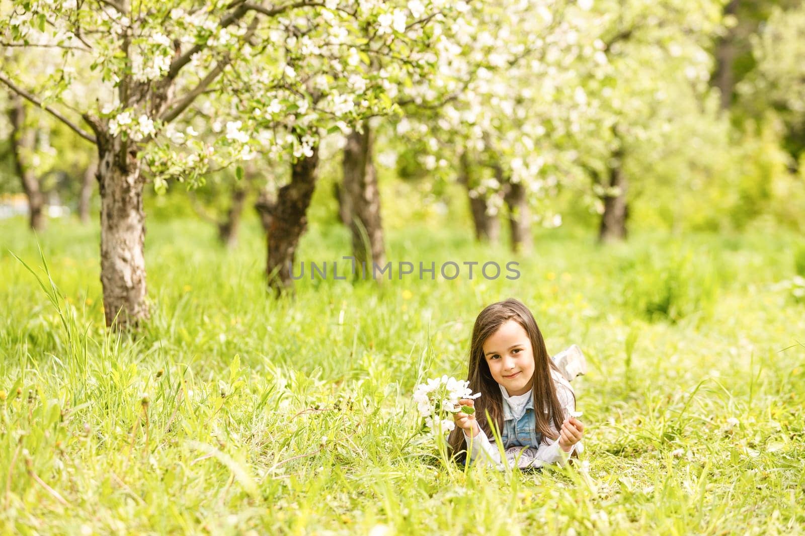 Portrait of cute and pretty little girl in spring blooming trees. Adorable little girl smiling in blooming garden on sunny day. Child and flowers. Childhood & natural tenderness. Children's day.