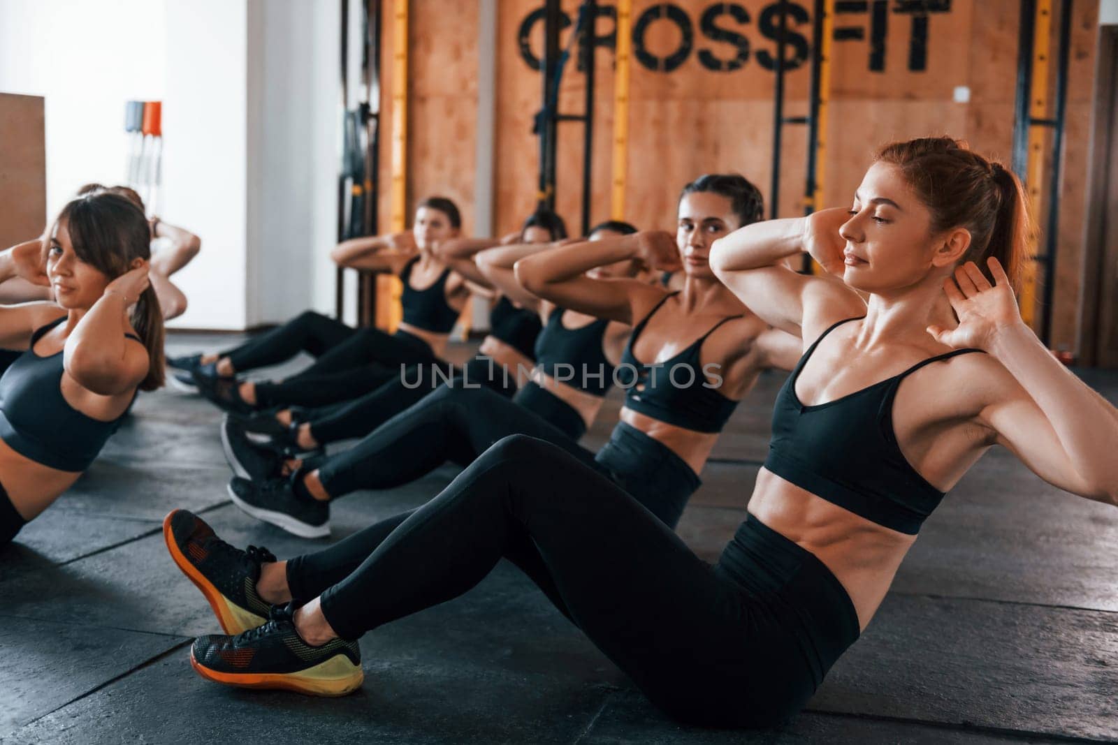 Doing abs. Group of young sportive people have crossfit day indoors in gym.
