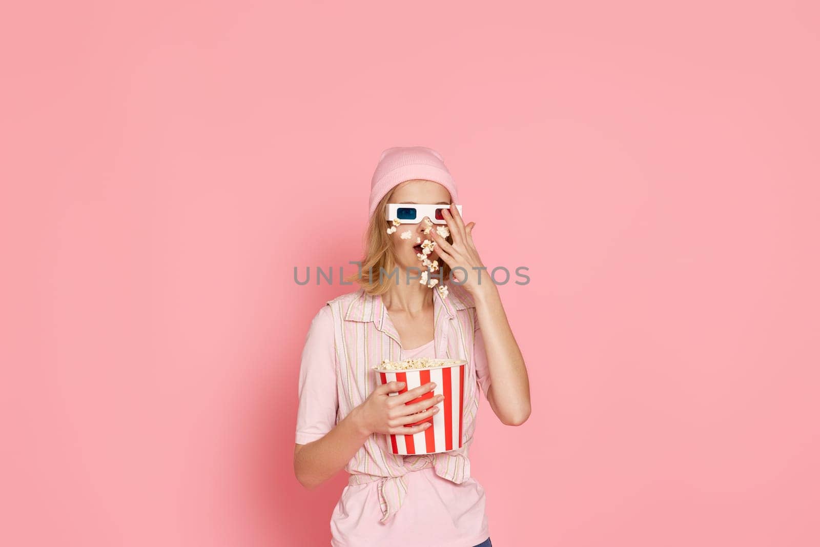 surprised girl with short haircut holding bucket of popcorn on pink background